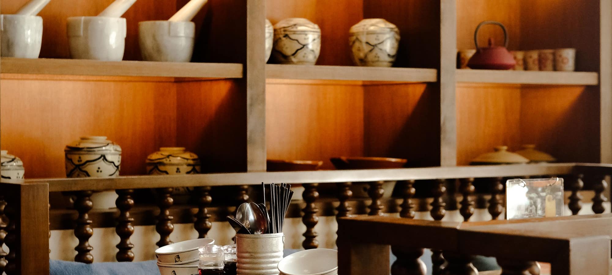 A warm Asian restaurant interior with ceramics on wooden shelves