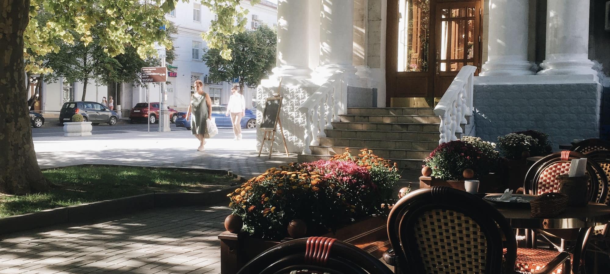 A sunlit street terrace with café tables and chairs
